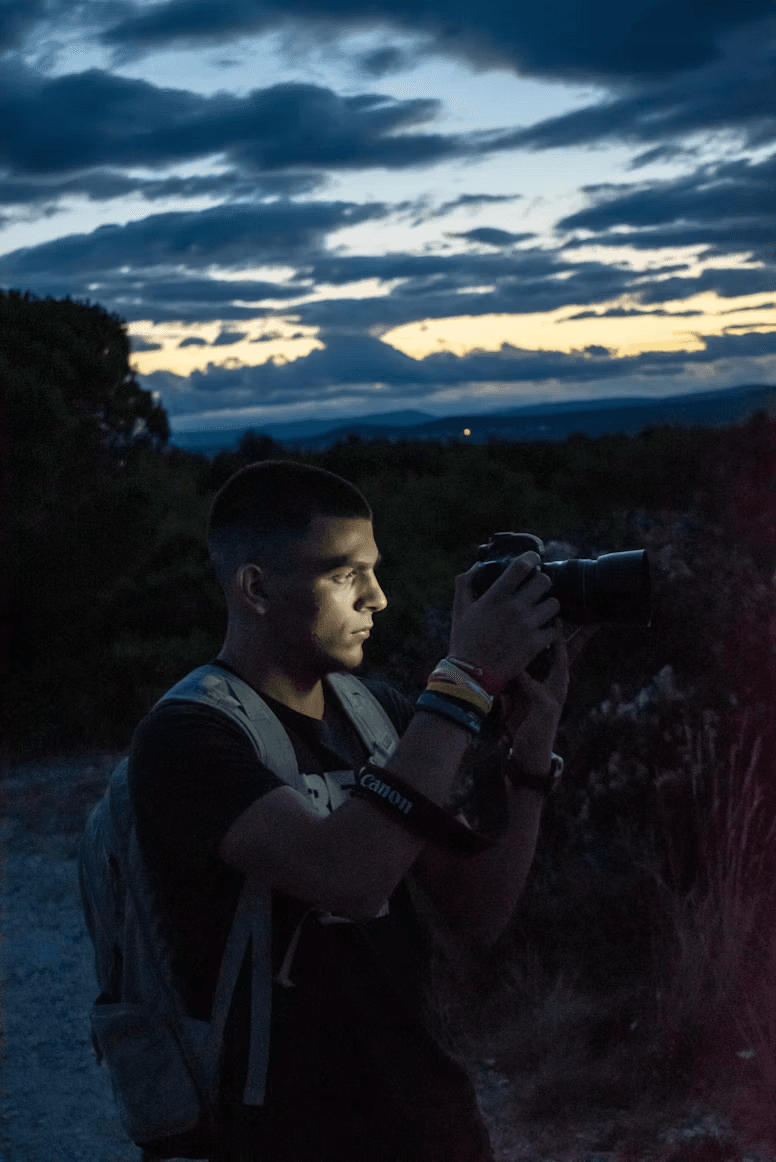 Një fotograf duke mbajtur një kamerë dhe duke fotografuar një peizazh në muzg